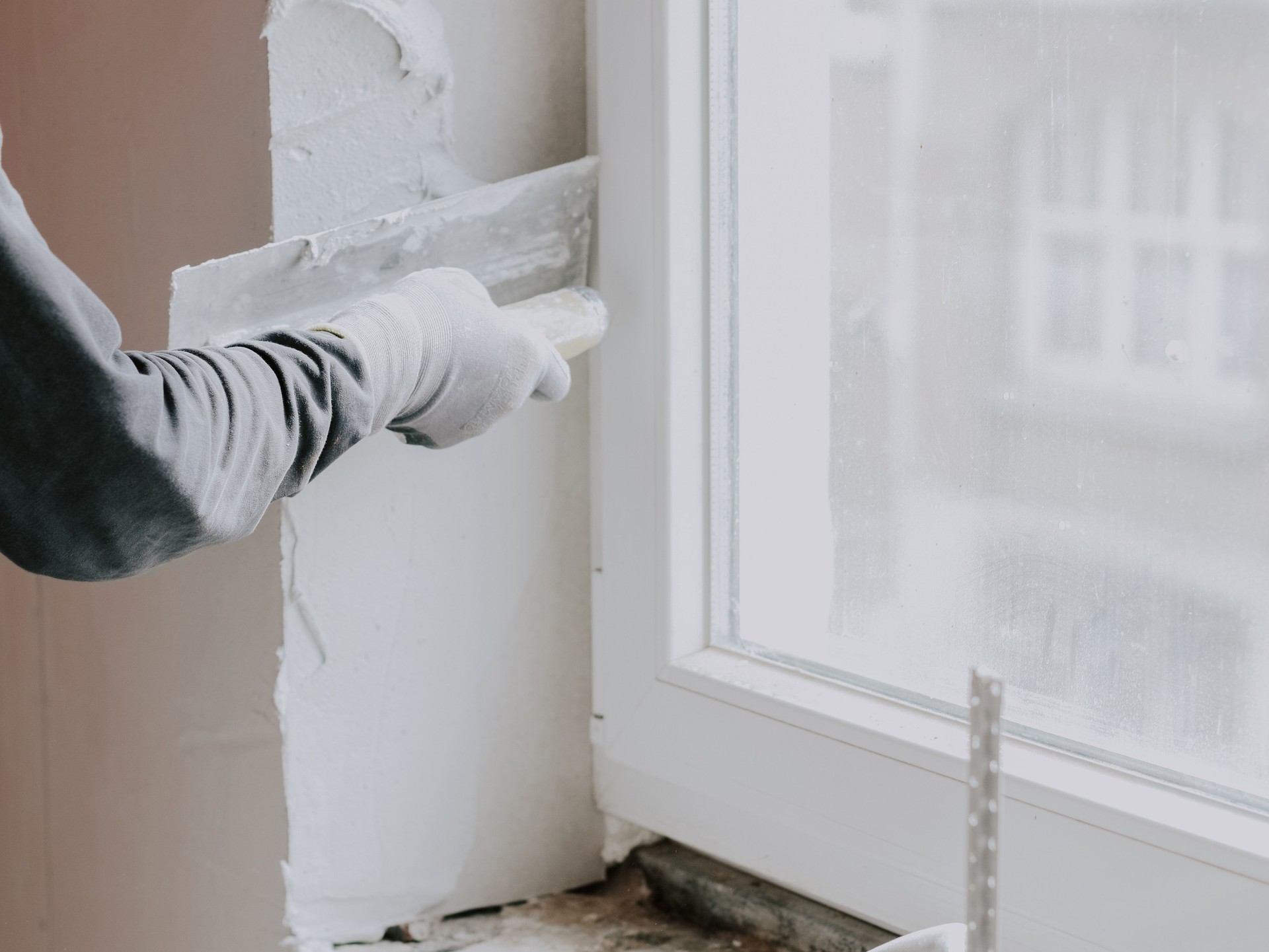 La main d’un gars applique du mastic frais avec une petite spatule sur l’ouverture de la fenêtre