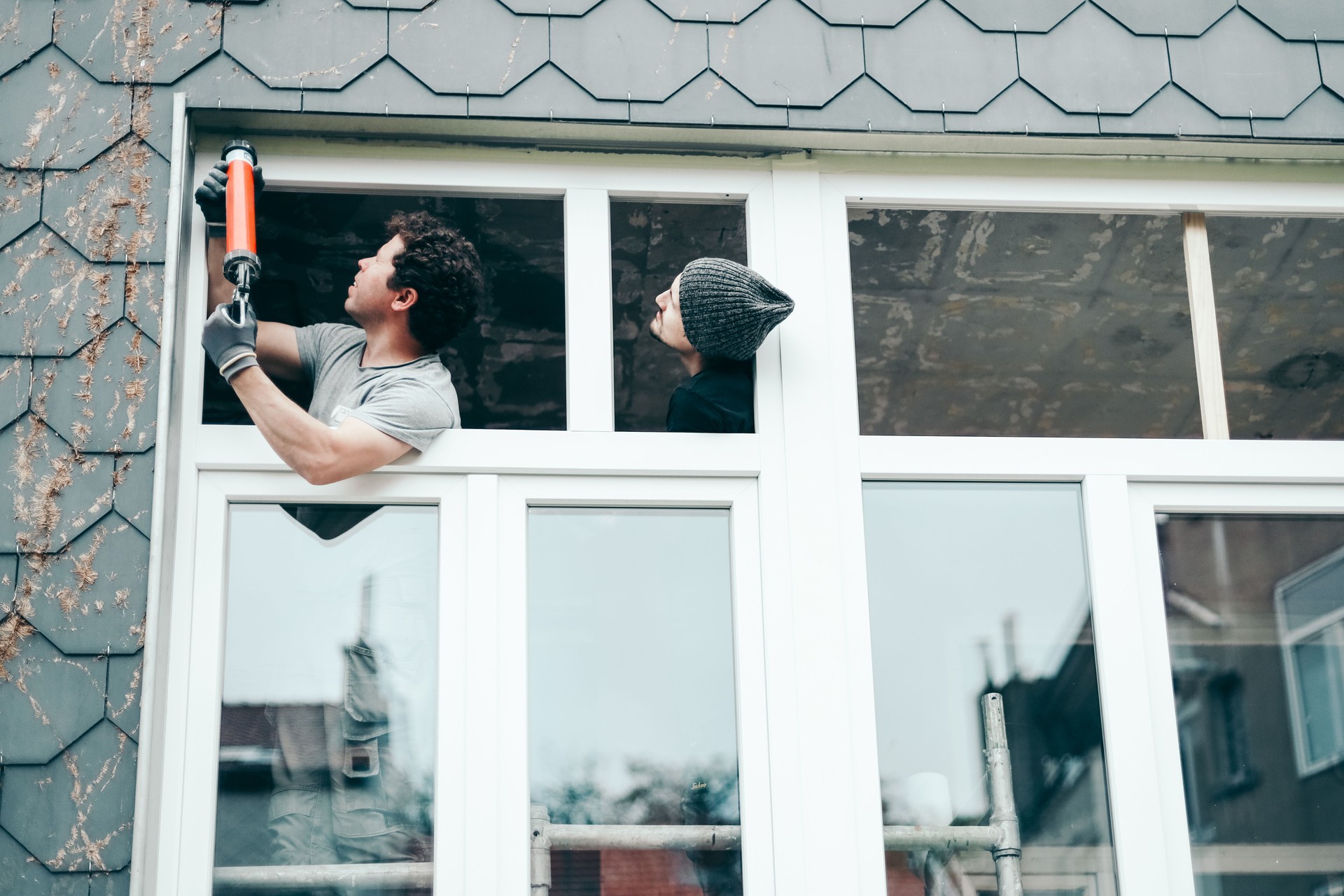 Two people repair windows using silicone.
